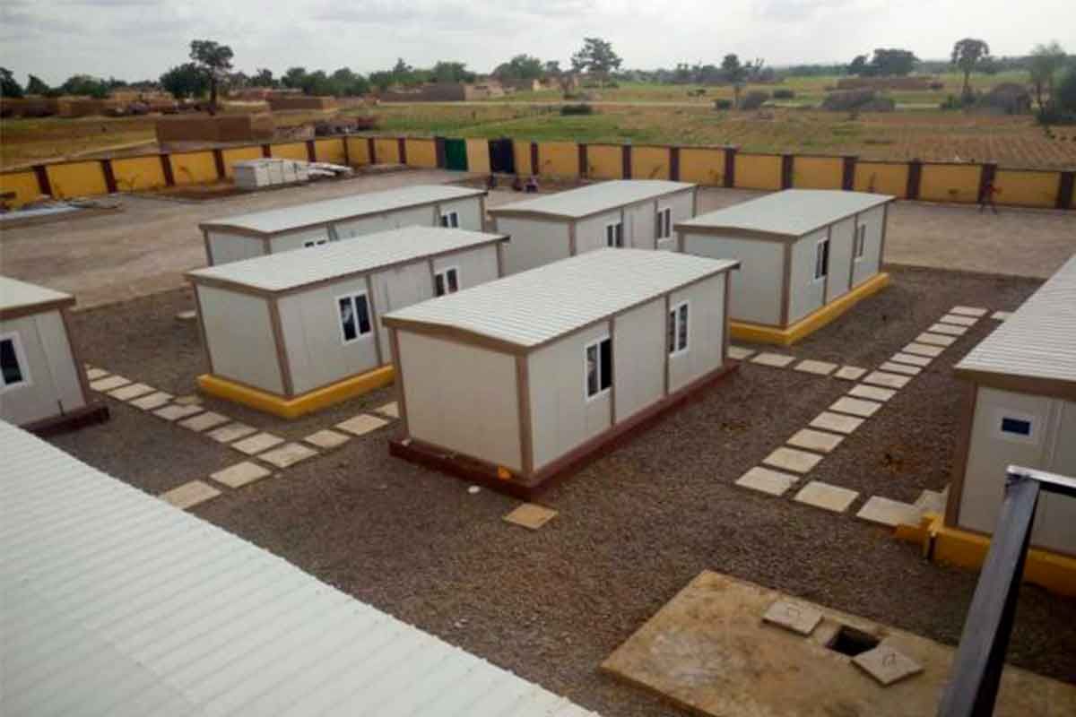 Elevated view of a container camp of single-storey units arranged around paved walkways inside a walled compound.