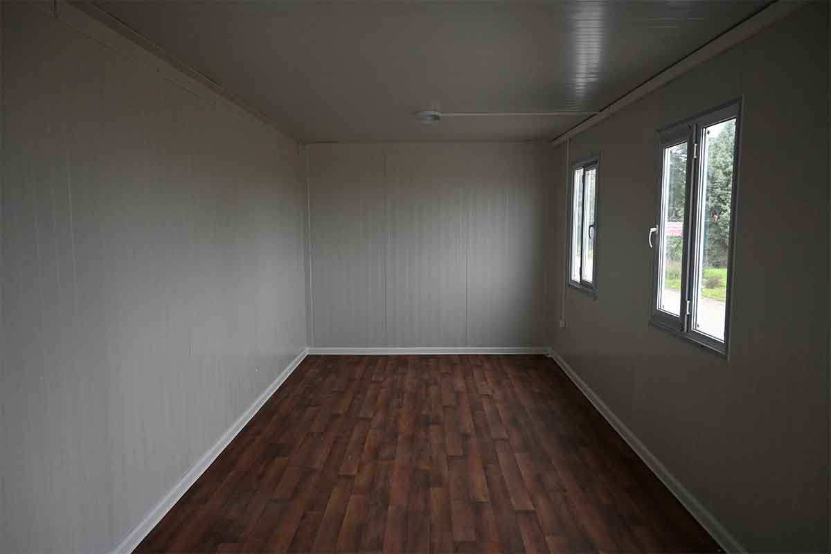 Empty interior of a standard container unit, with lined walls, wood-effect flooring and two windows.
