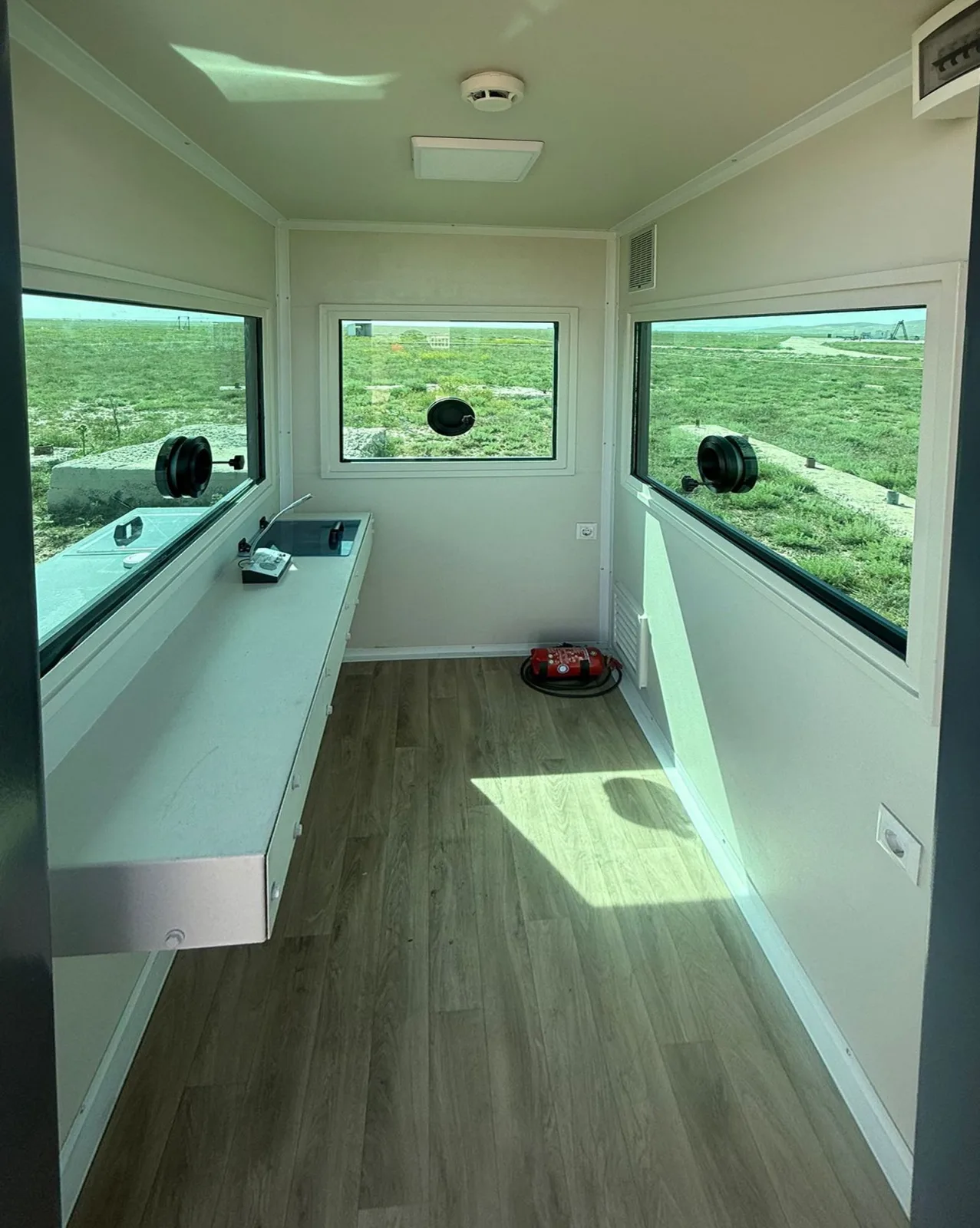 Interior of an armoured cabin, with a full-length worktop, wood-effect flooring and ballistic windows fitted with firing ports on three sides.