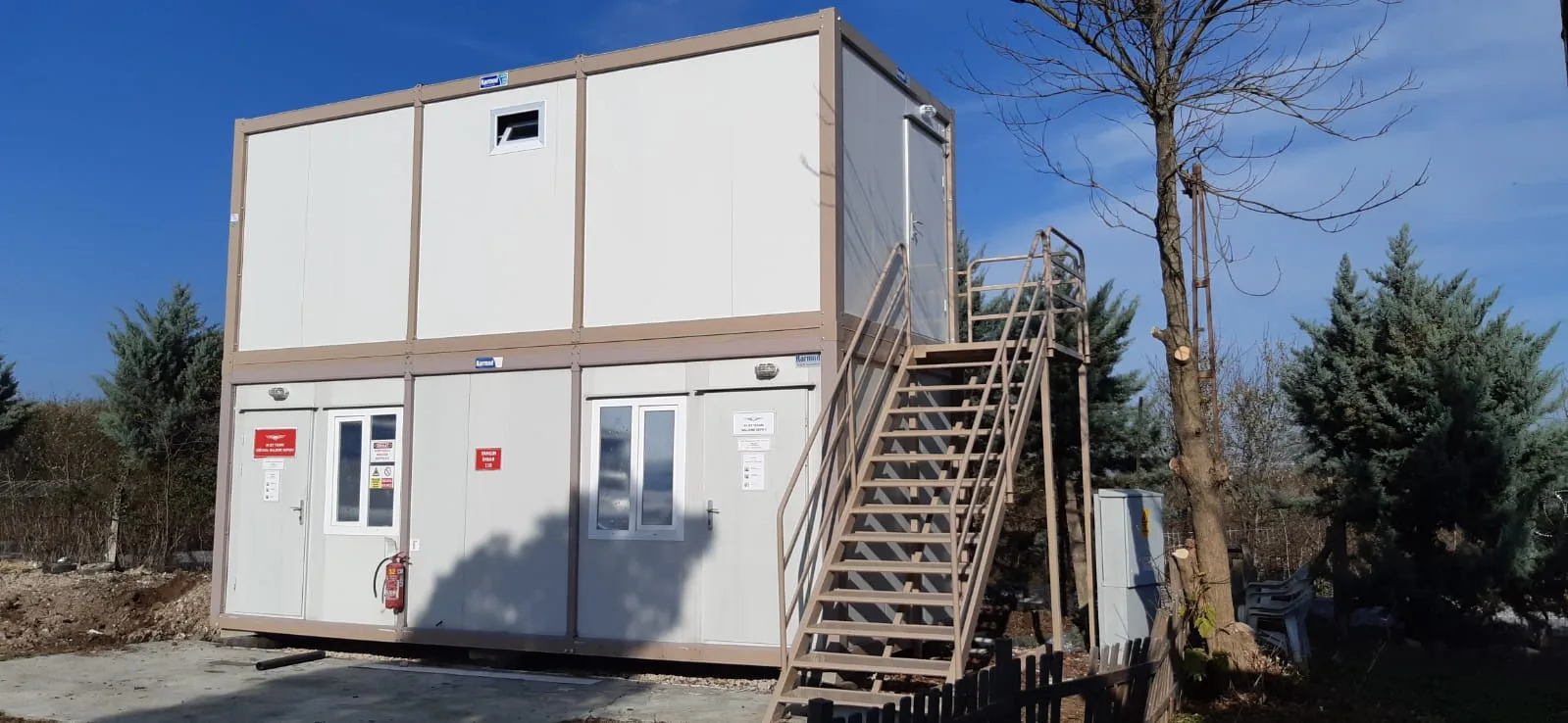 Two-storey white and beige container office block with an external steel staircase to the upper floor.