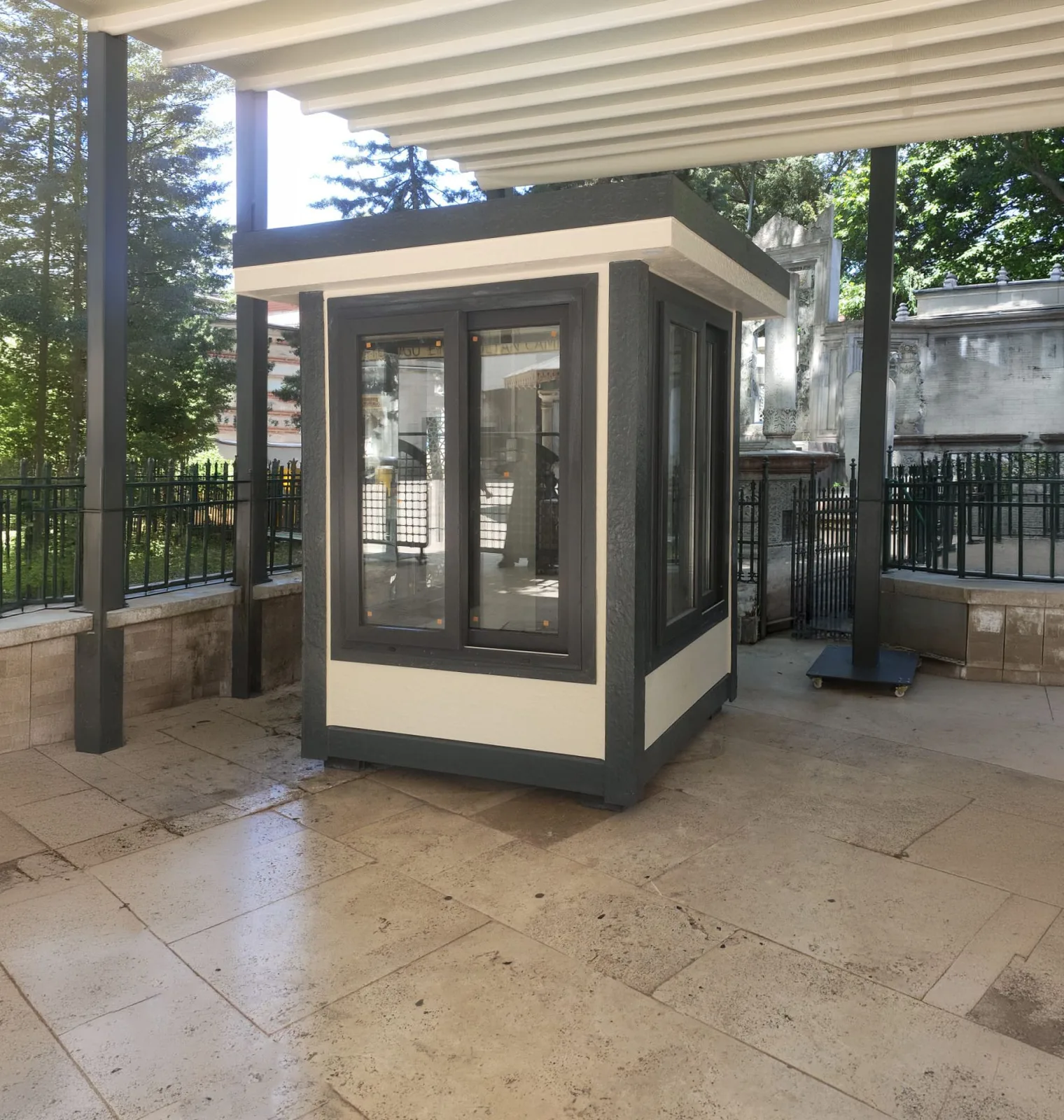 Dark grey and cream Metro City cabin standing under a pergola canopy on travertine paving in a walled courtyard.