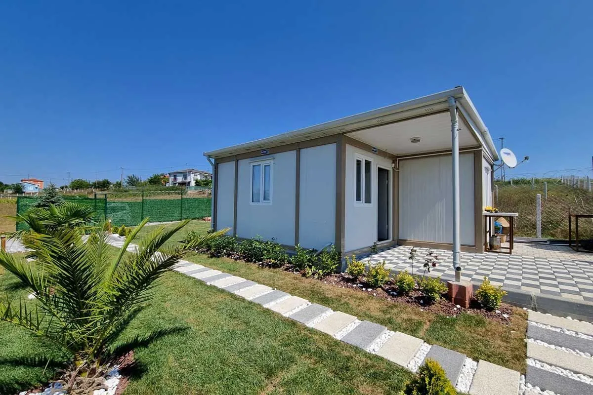 Container house with a canopied terrace, block paving and planted borders in a landscaped garden.