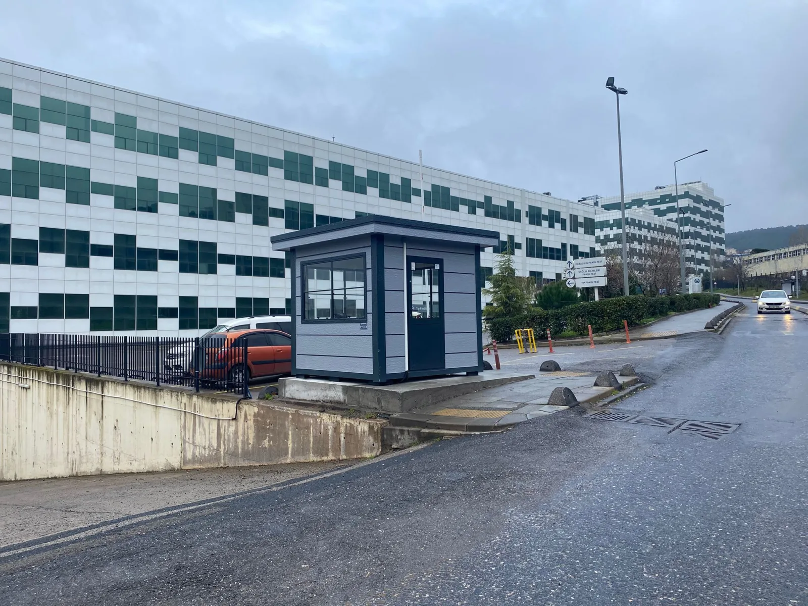 Grey Metro City gatehouse beside the vehicle entrance to a university campus on a wet winter morning.