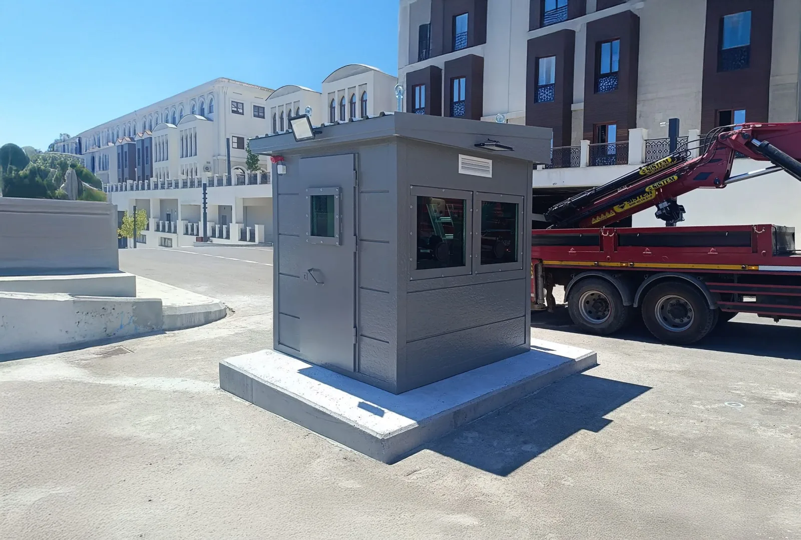 Grey armoured security cabin on a concrete plinth at a financial centre, with the delivery crane still alongside.