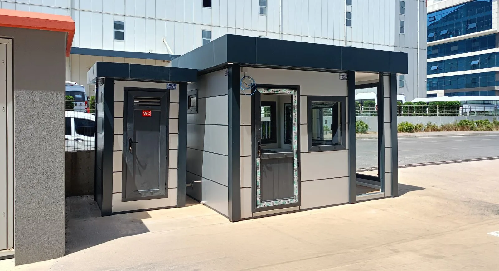 Grey Metro City cabin with a canopy and a separate WC cubicle alongside, at the entrance to an industrial site.