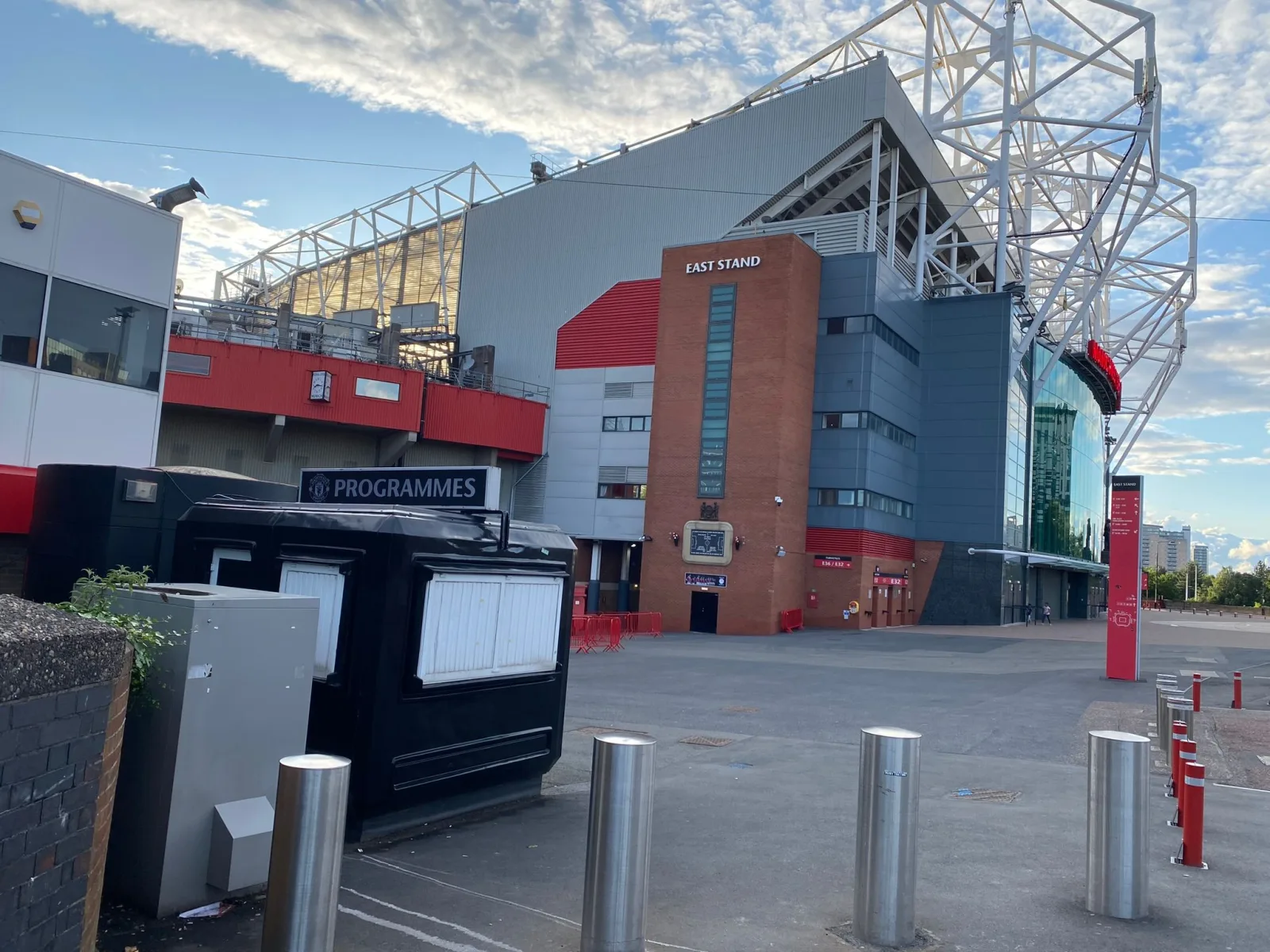 Black Manchester United programme kiosk with the brick East Stand of Old Trafford rising behind it.