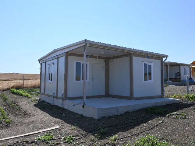 Container house raised on a concrete slab beside harvested farmland, clear of the irrigated ground