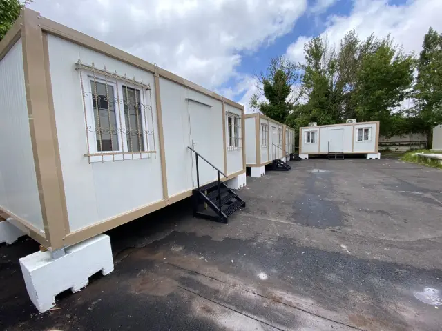 Three separate container offices standing side by side on a paved yard in Spain, each with its own steps and door