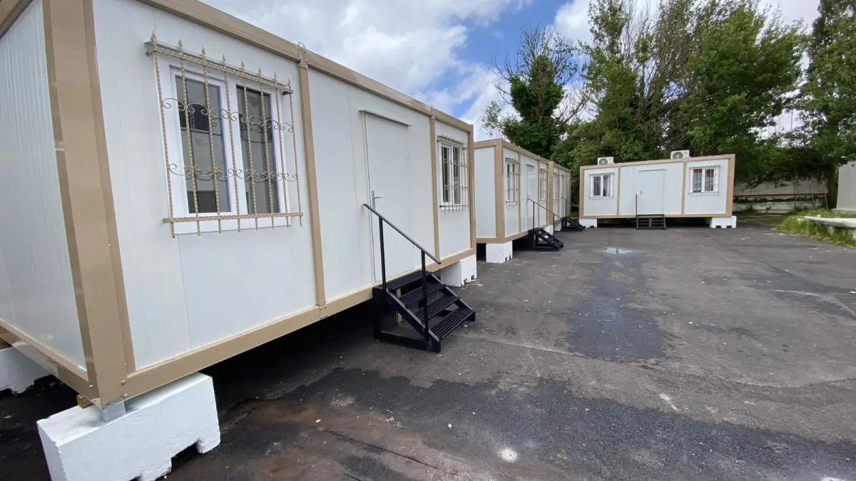 Three separate container offices standing side by side on a paved yard in Spain, each with its own steps and door