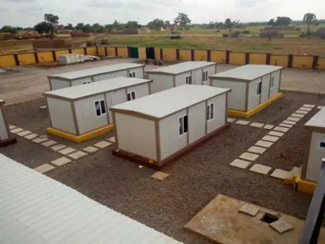 Elevated view of a walled compound with single-storey container units laid out around paved walkways