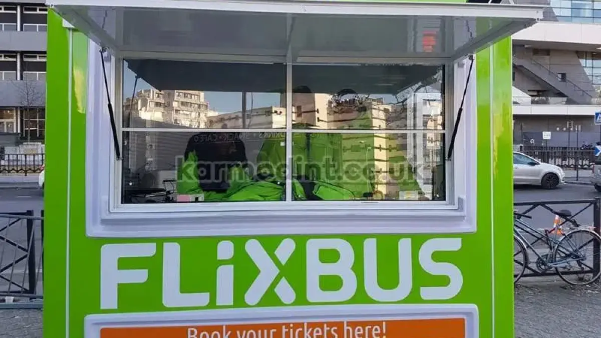 Green FlixBus GRP ticket kiosk with its top-hinged serving hatch raised on gas struts over the counter window