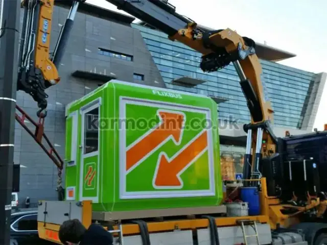 Green FlixBus GRP ticket kiosk with brand graphics on its delivery lorry, under the lorry-mounted crane