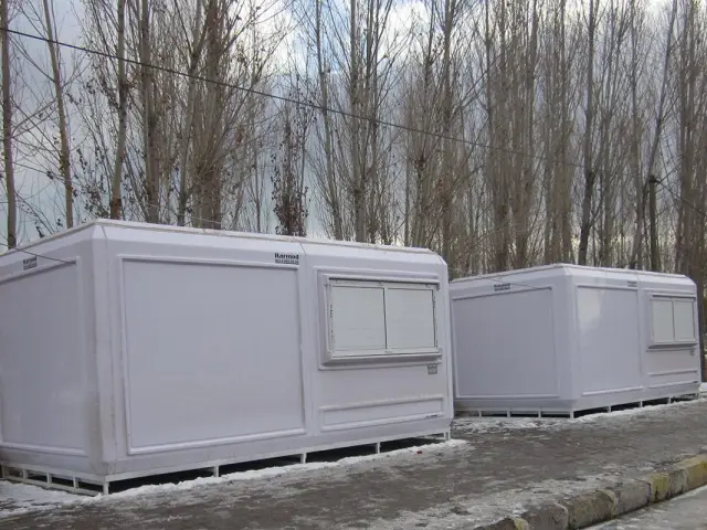 Two white GRP cabins on steel skids at a roadside in winter, with snow on the ground
